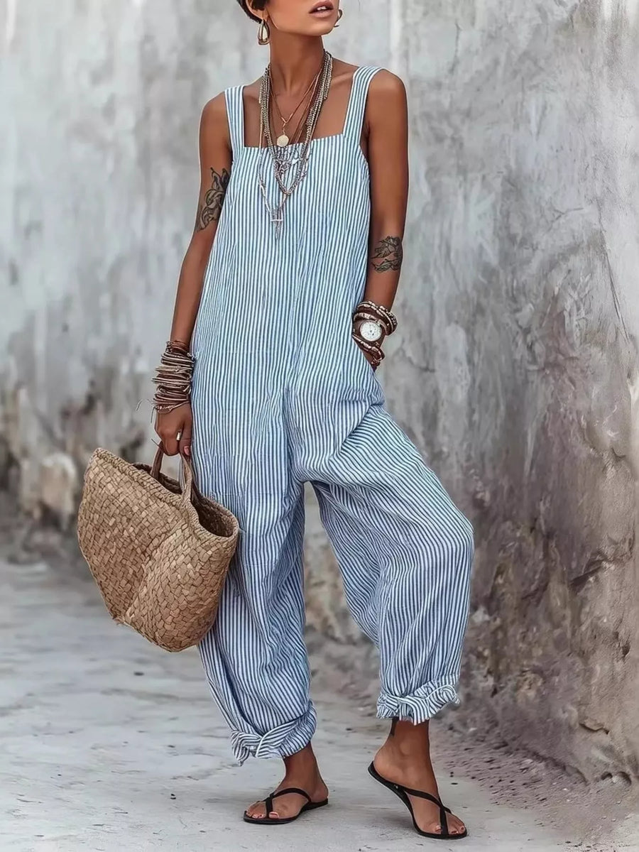 Woman wearing a blue striped jumpsuit holding a woven bag against a textured wall.