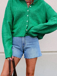 Person wearing a green cardigan and denim shorts against a neutral background