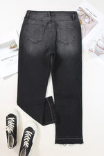 Black jeans on a white surface with sneakers and a newspaper.