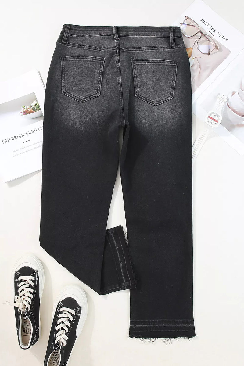 Black jeans on a white surface with sneakers and a newspaper.