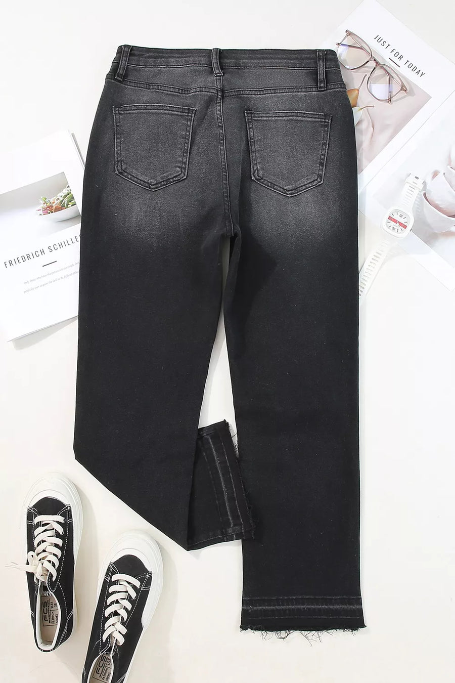 Black jeans on a white surface with sneakers and a newspaper.