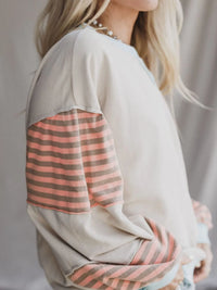 Close-up of a person wearing a light-colored sweater with striped sleeves against a neutral background