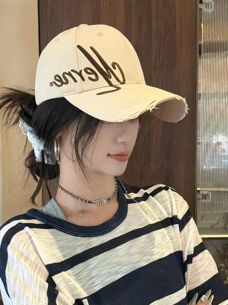 Person wearing a beige cap with text and a striped shirt indoors.