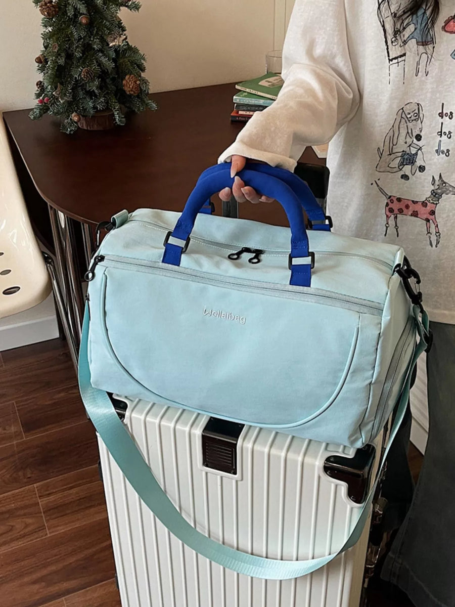 Light blue bag with blue handles held over a white suitcase indoors.