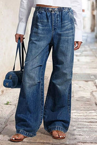 Person wearing wide-leg jeans holding a blue handbag on a stone pavement.