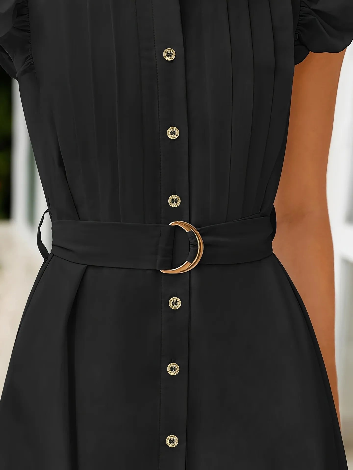Black dress with gold buttons and belt on a blurred background