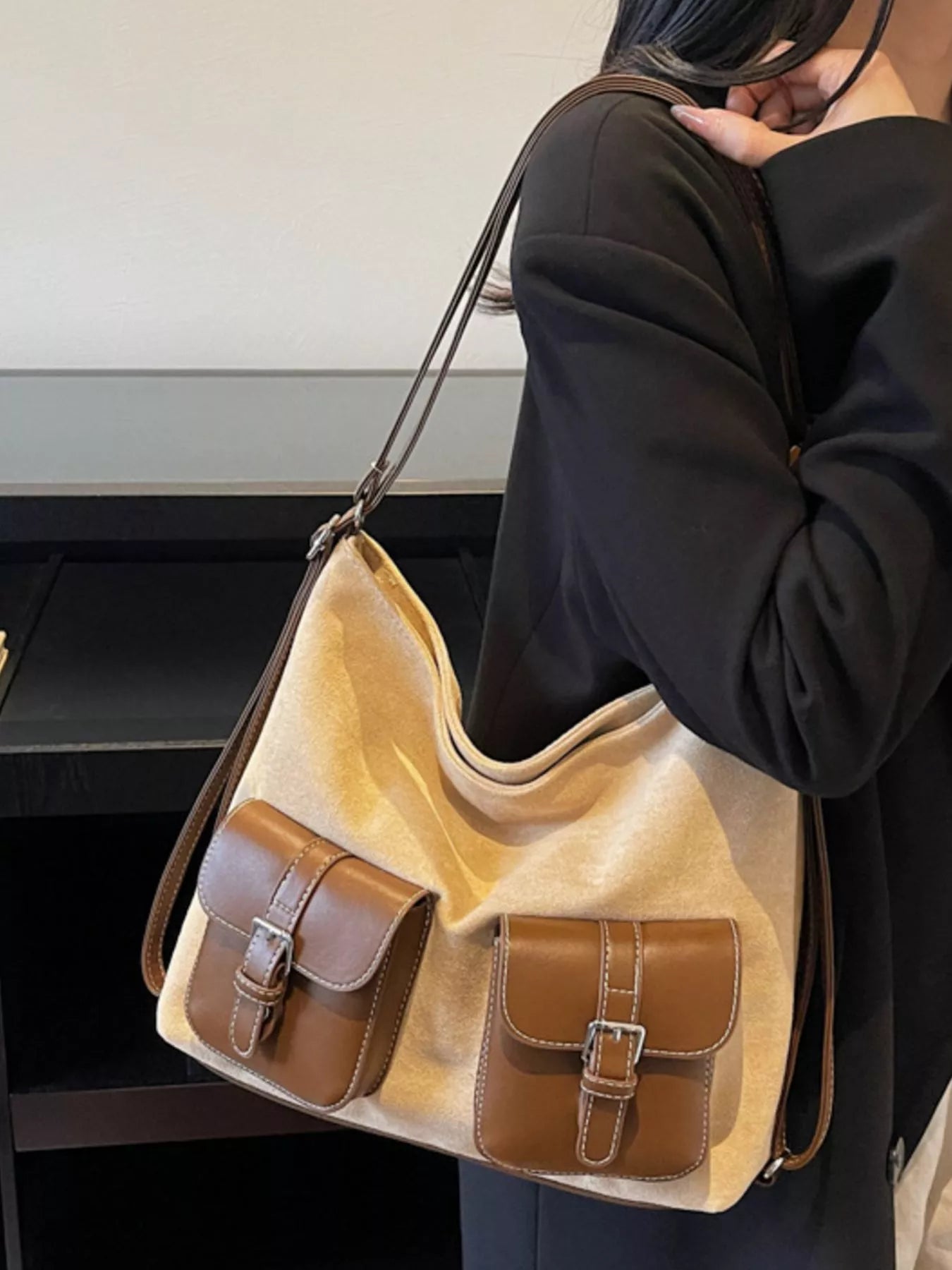 Beige handbag with brown accents held by a person wearing a black jacket.