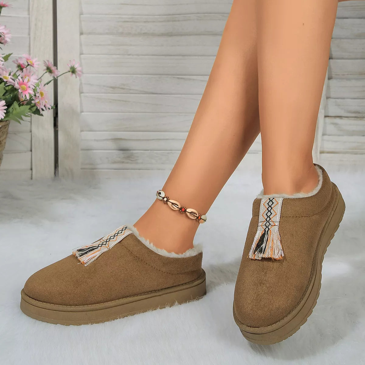 Brown slippers with tassels worn by a person on a light background