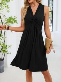 Woman wearing a black sleeveless dress holding a clutch indoors.