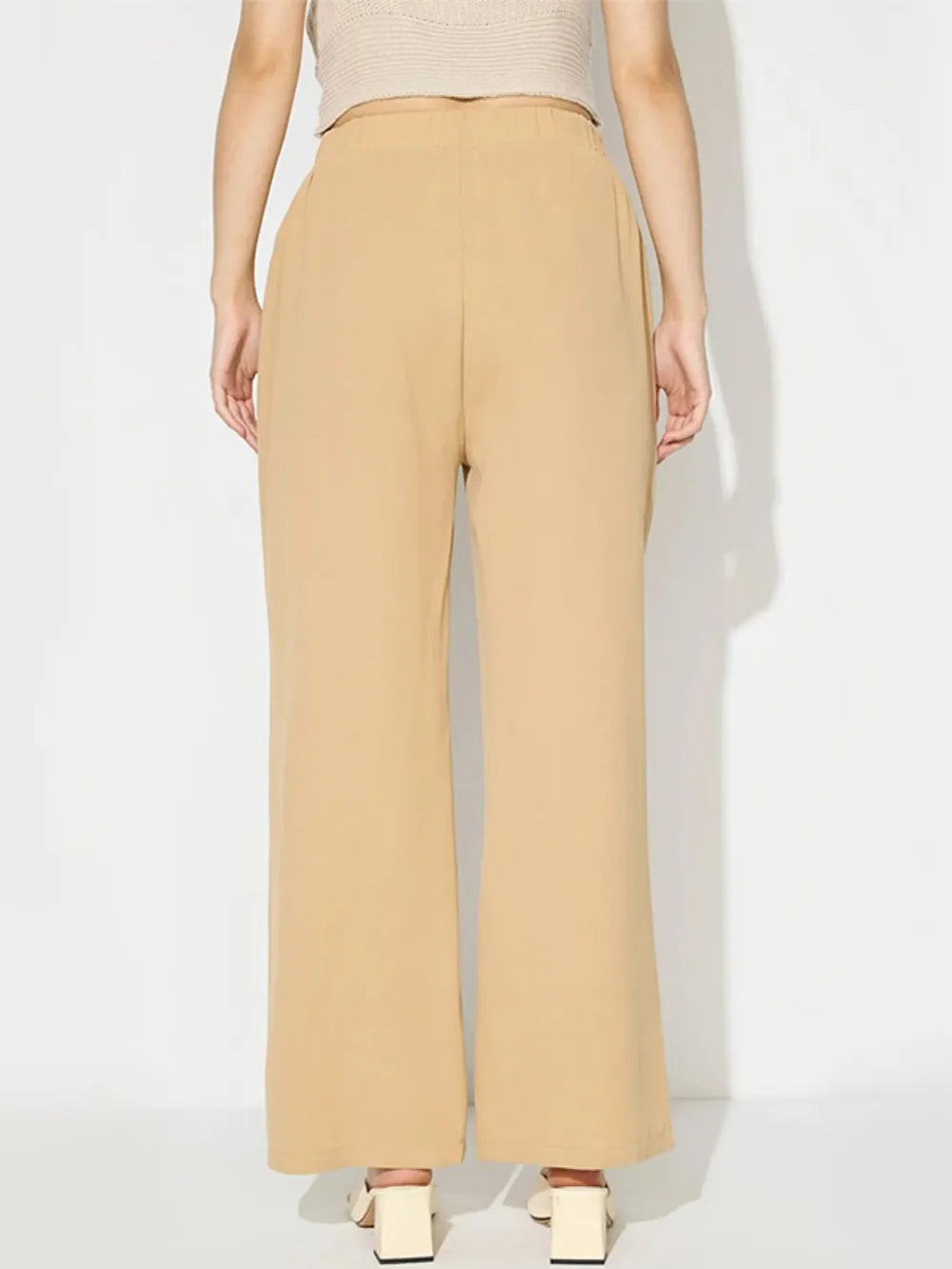 Person wearing beige high-waisted pants on a white background