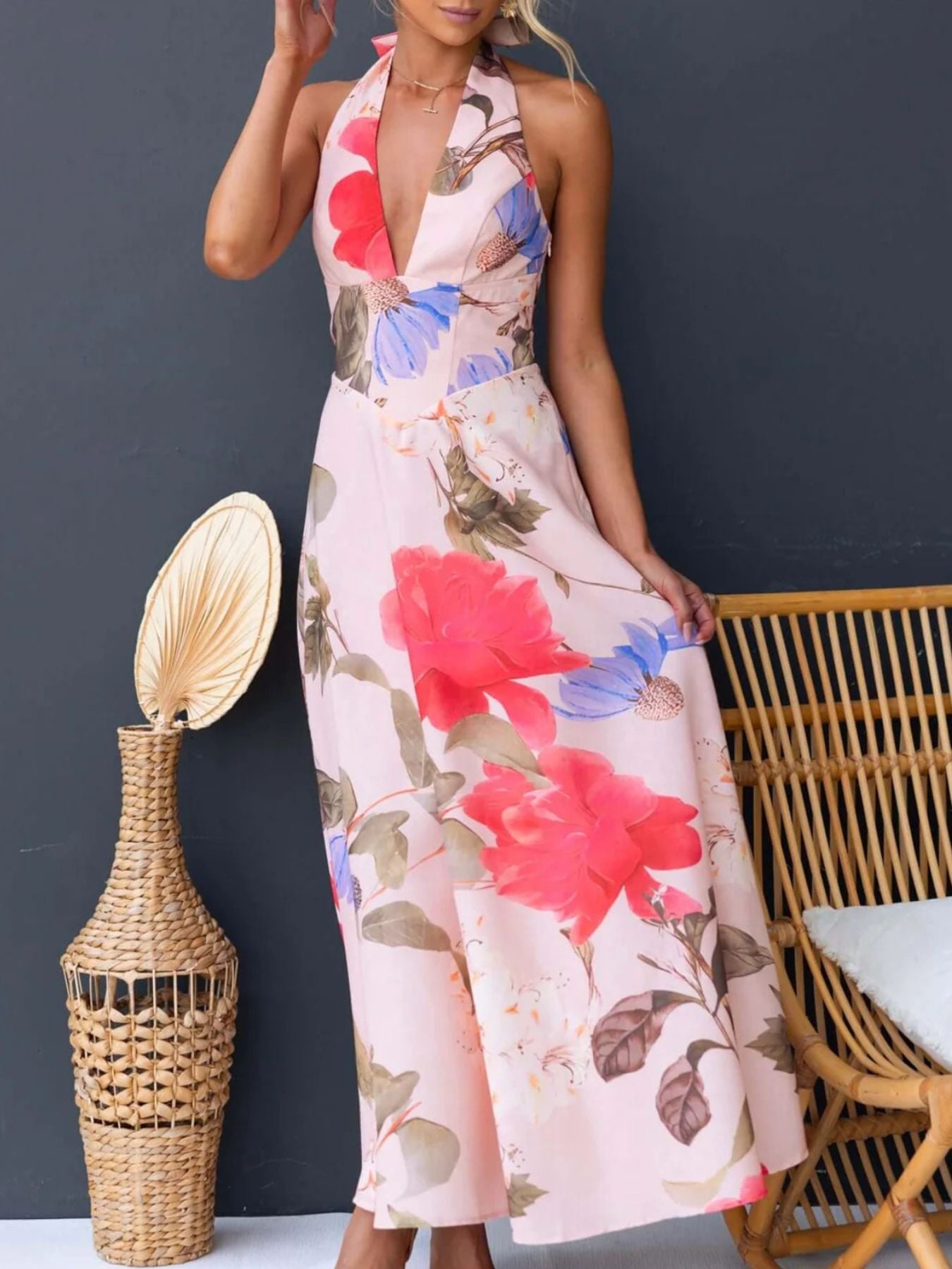 Woman wearing a floral dress with a dark gray background, wicker chair, and decorative vase.