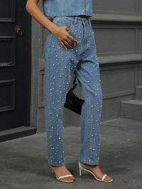 Person wearing blue jeans with pearl embellishments standing on steps.