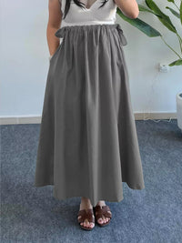 Person wearing a gray skirt in an indoor setting with a plant in the background