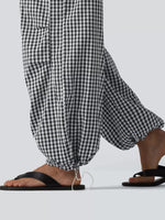 Black and white gingham checkered wide-leg pants with drawstring hems, shown on a model wearing black flip-flop sandals against a light gray background.