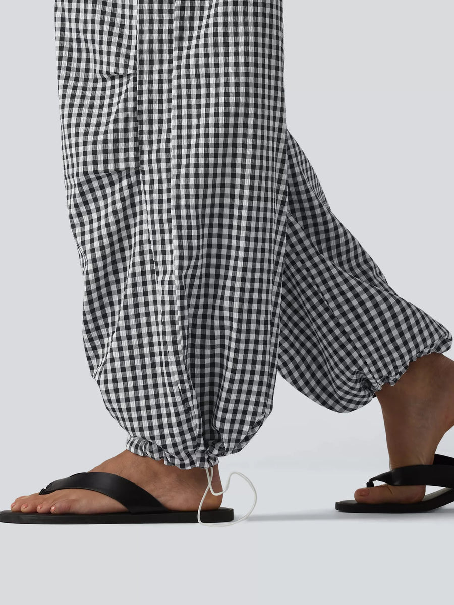 Black and white gingham checkered wide-leg pants with drawstring hems, shown on a model wearing black flip-flop sandals against a light gray background.