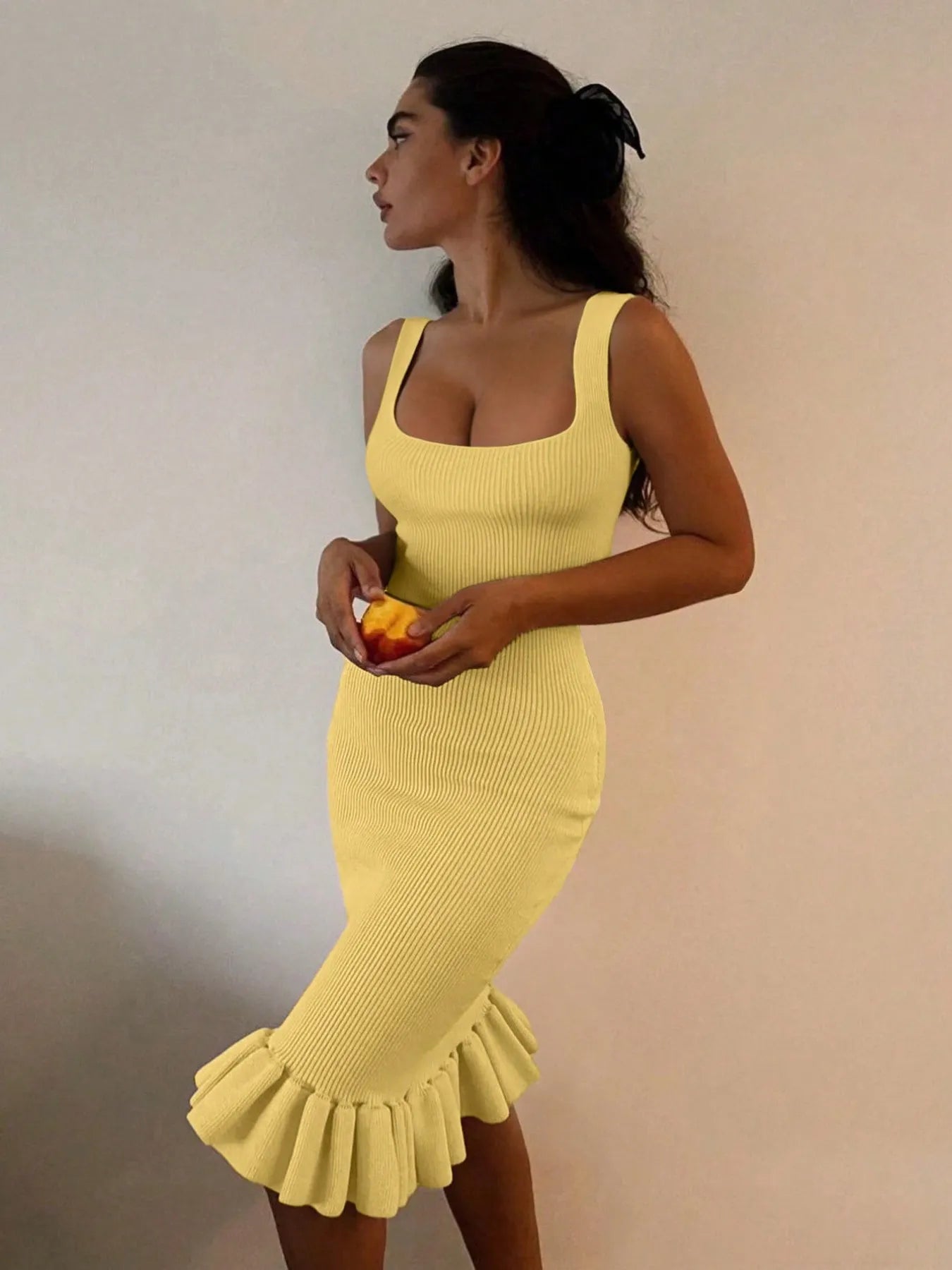 Woman wearing a yellow dress with ruffled hem against a plain background