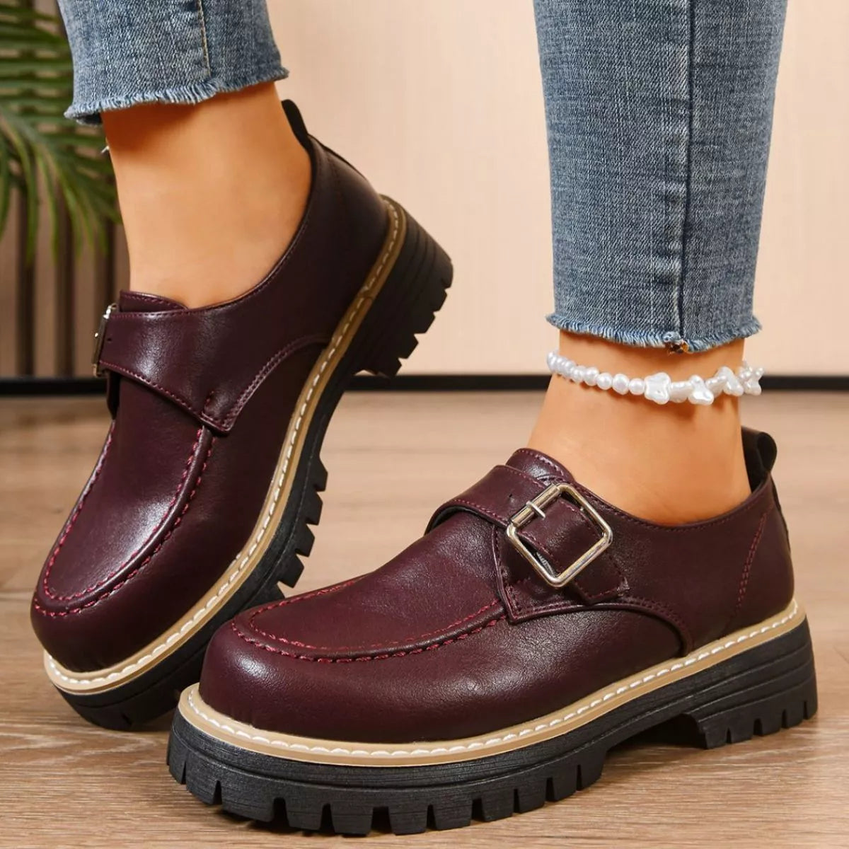 Brown leather shoes with buckles worn with blue jeans on a wooden floor.