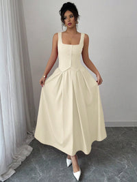 Woman wearing a beige sleeveless dress standing in a room with white curtains.
