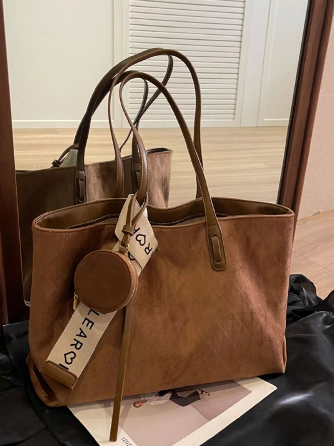 Brown leather handbag with a visible brand tag on a wooden floor.