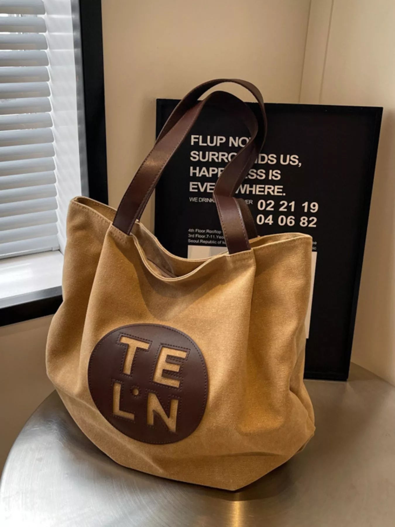 Beige tote bag with 'TE LN' logo on a metallic surface