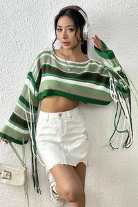 Woman wearing a green and brown striped sweater with white shorts against a white wall.