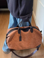 Person holding a brown leather duffel bag indoors.