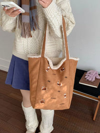 Person holding a brown tote bag with dog prints, wearing a cream sweater and blue skirt.