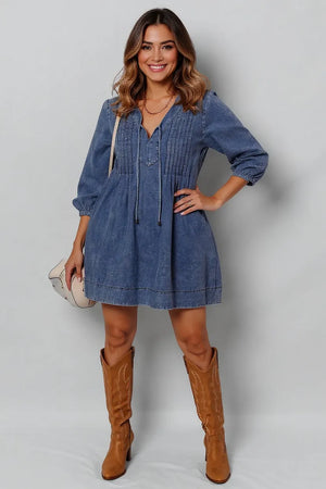 Woman wearing a blue denim dress and brown boots against a plain background