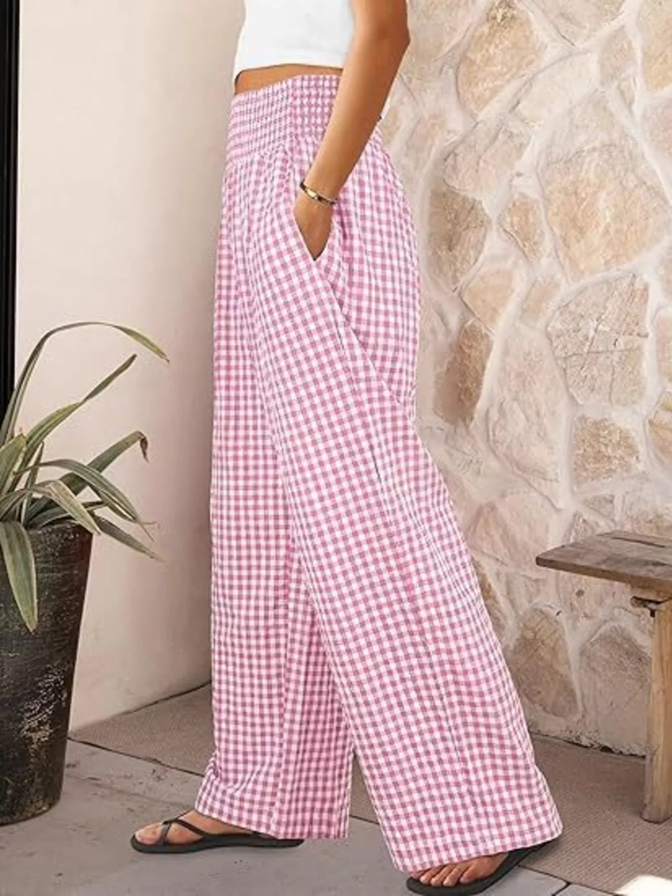 Person wearing pink checkered pants standing against a stone wall.