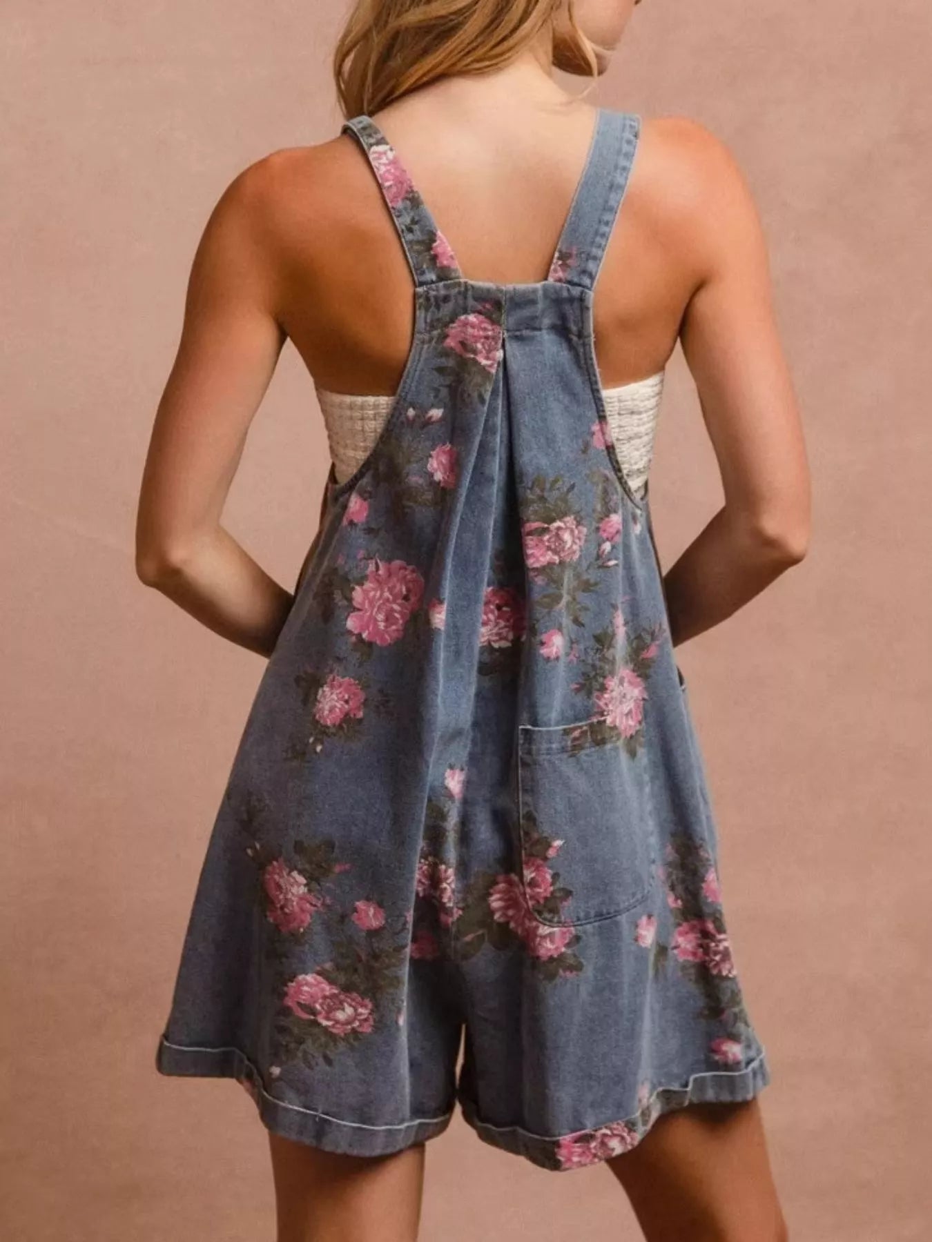Denim overalls with floral pattern worn by a person on a beige background