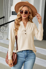 Woman wearing a beige long-sleeve shirt, blue jeans, and a brown hat outdoors.
