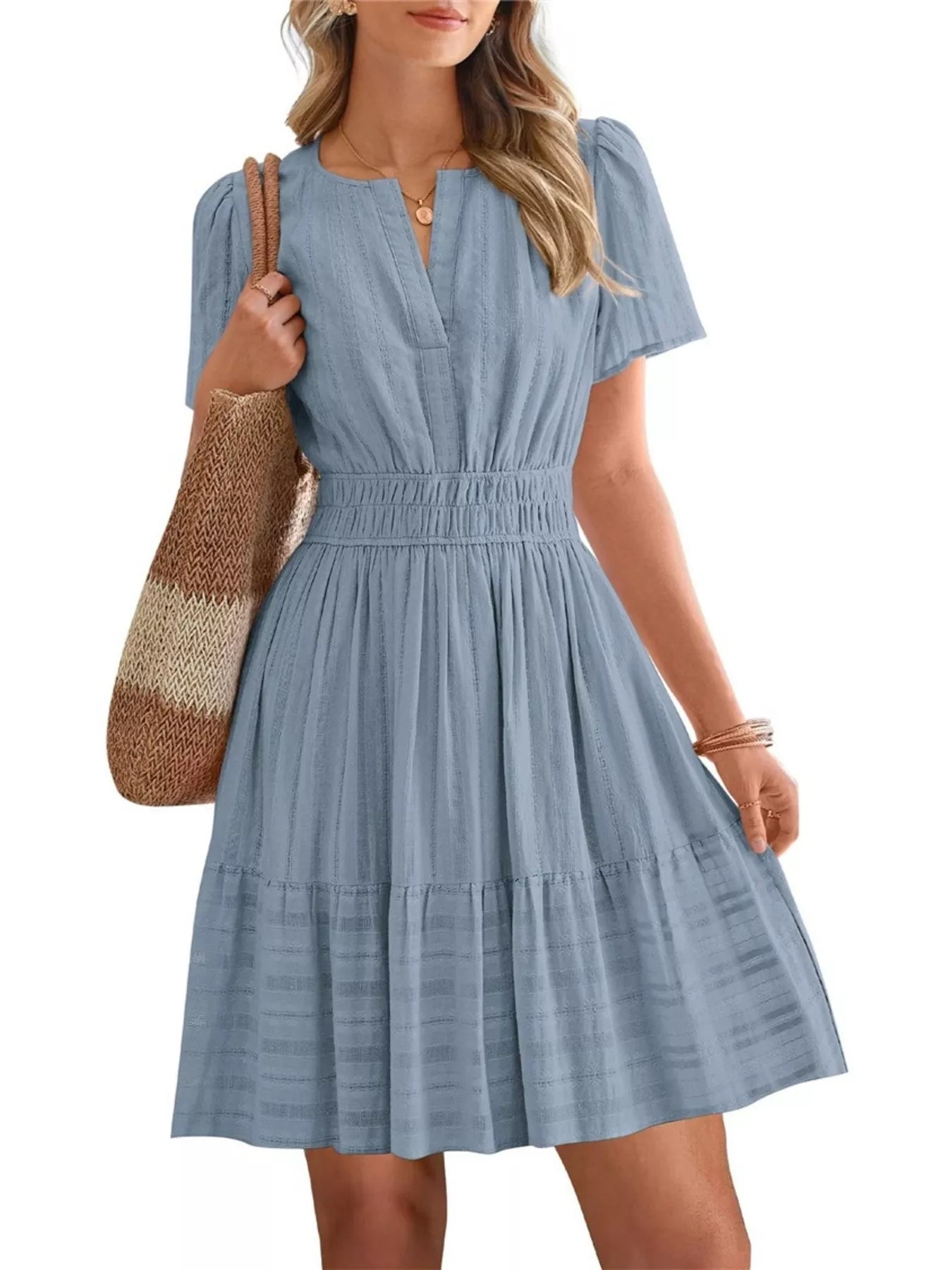 Woman wearing a blue dress holding a woven bag on a white background