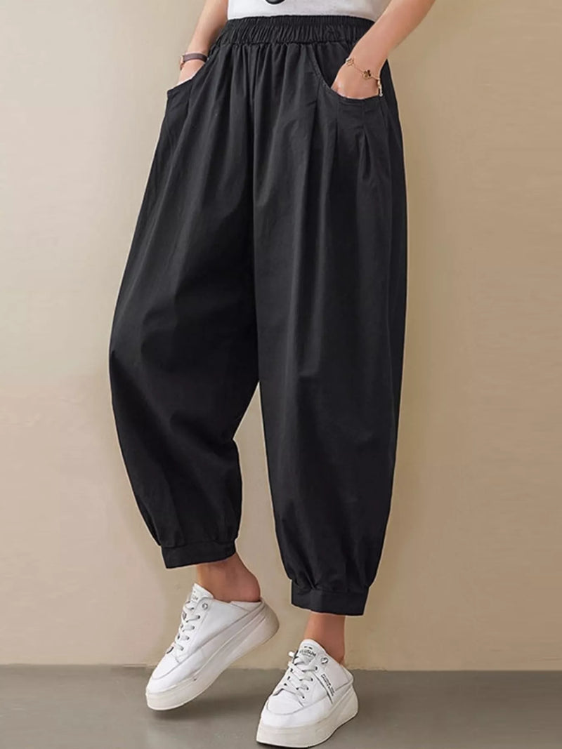 Person wearing black wide-leg pants and white sneakers on a beige background