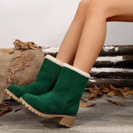 Green suede boots with white fur lining worn by a person, on a rustic wooden background.