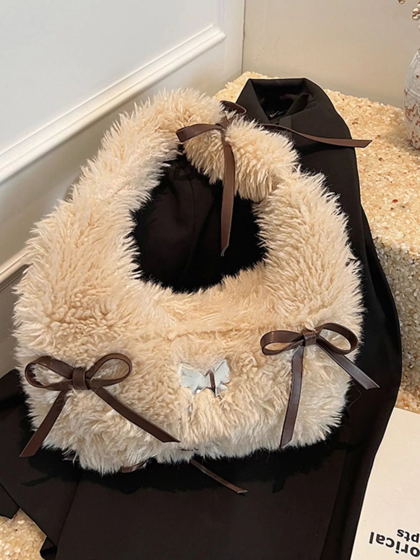 Fluffy beige pet bed with brown ribbons and a black bow on a white surface.