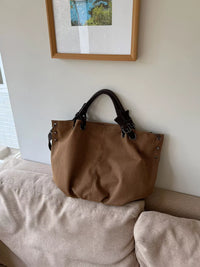 Brown handbag on a beige couch with a framed picture on the wall.