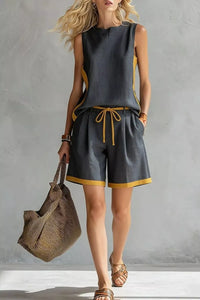 Woman wearing a gray sleeveless top and shorts with yellow accents, holding a woven bag against a gray background.