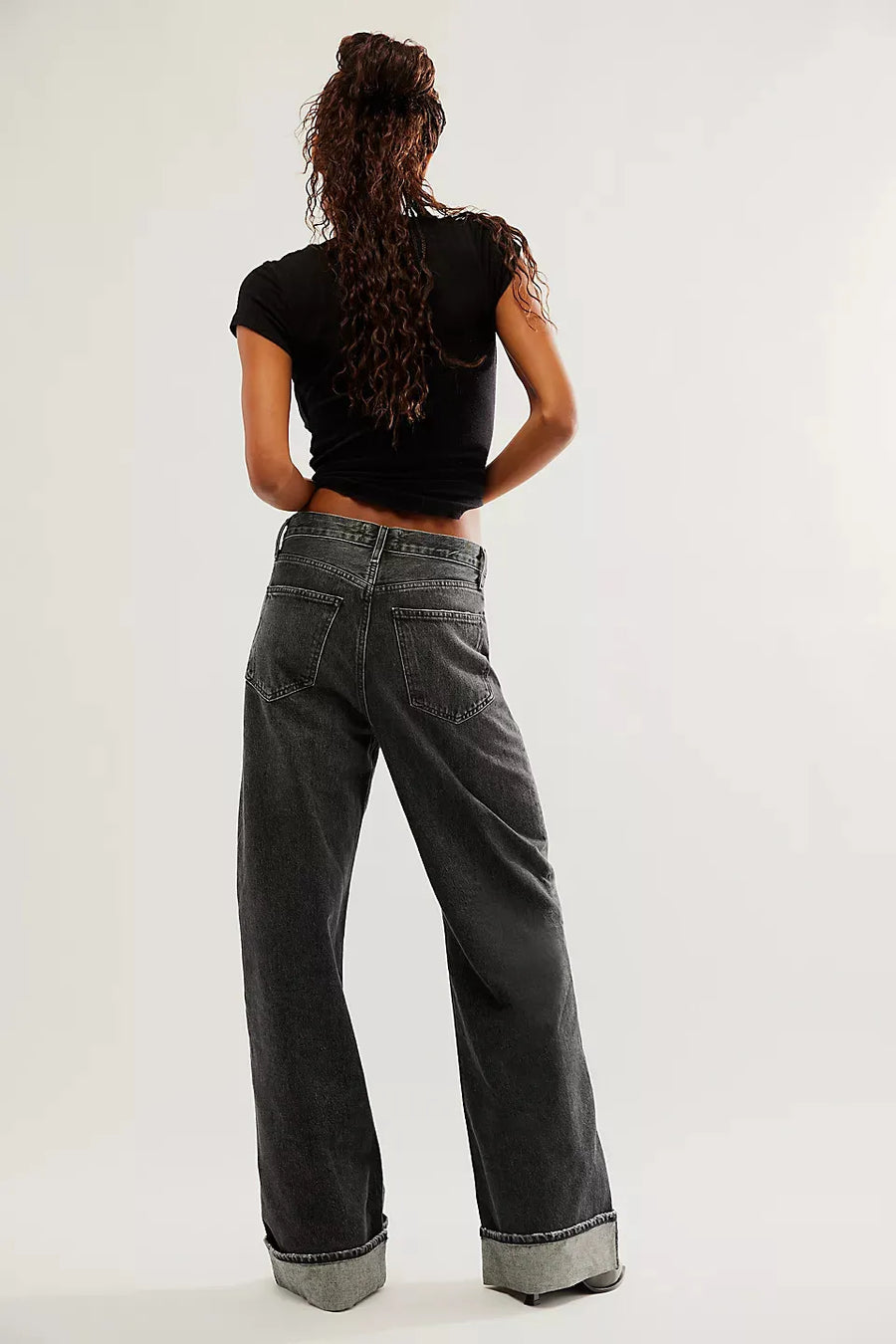 Person wearing black t-shirt and gray jeans from behind on a white background