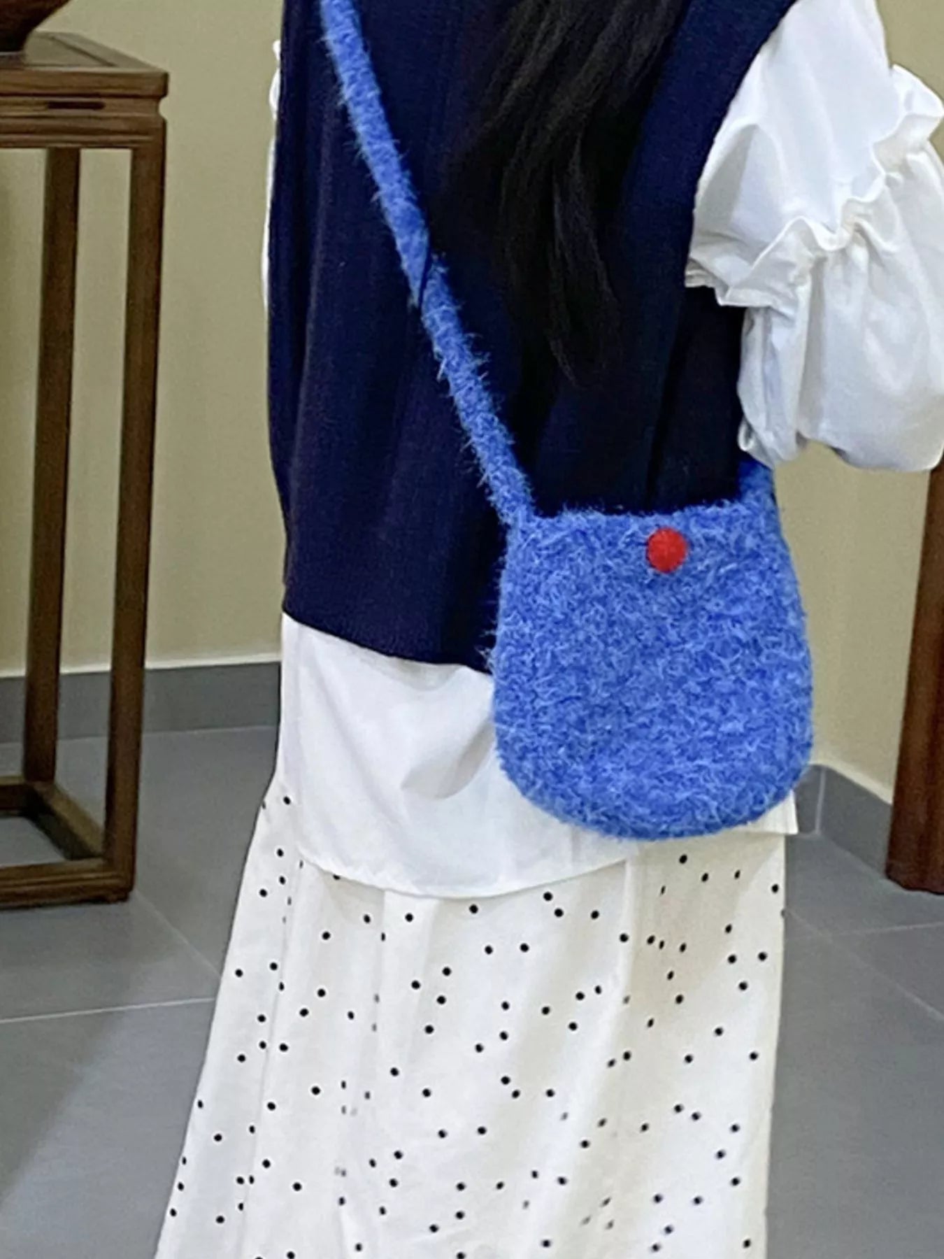 Person wearing a blue knitted bag with a red button on a neutral background