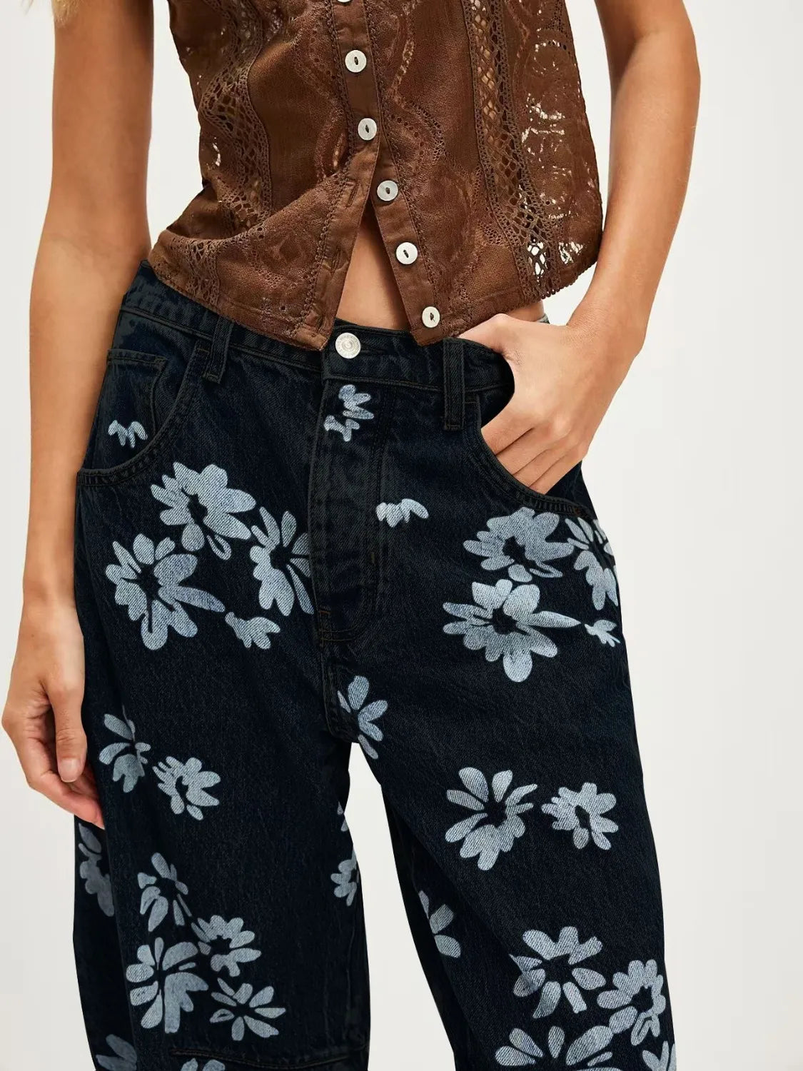 Person wearing a brown patterned top and black floral pants on a plain background