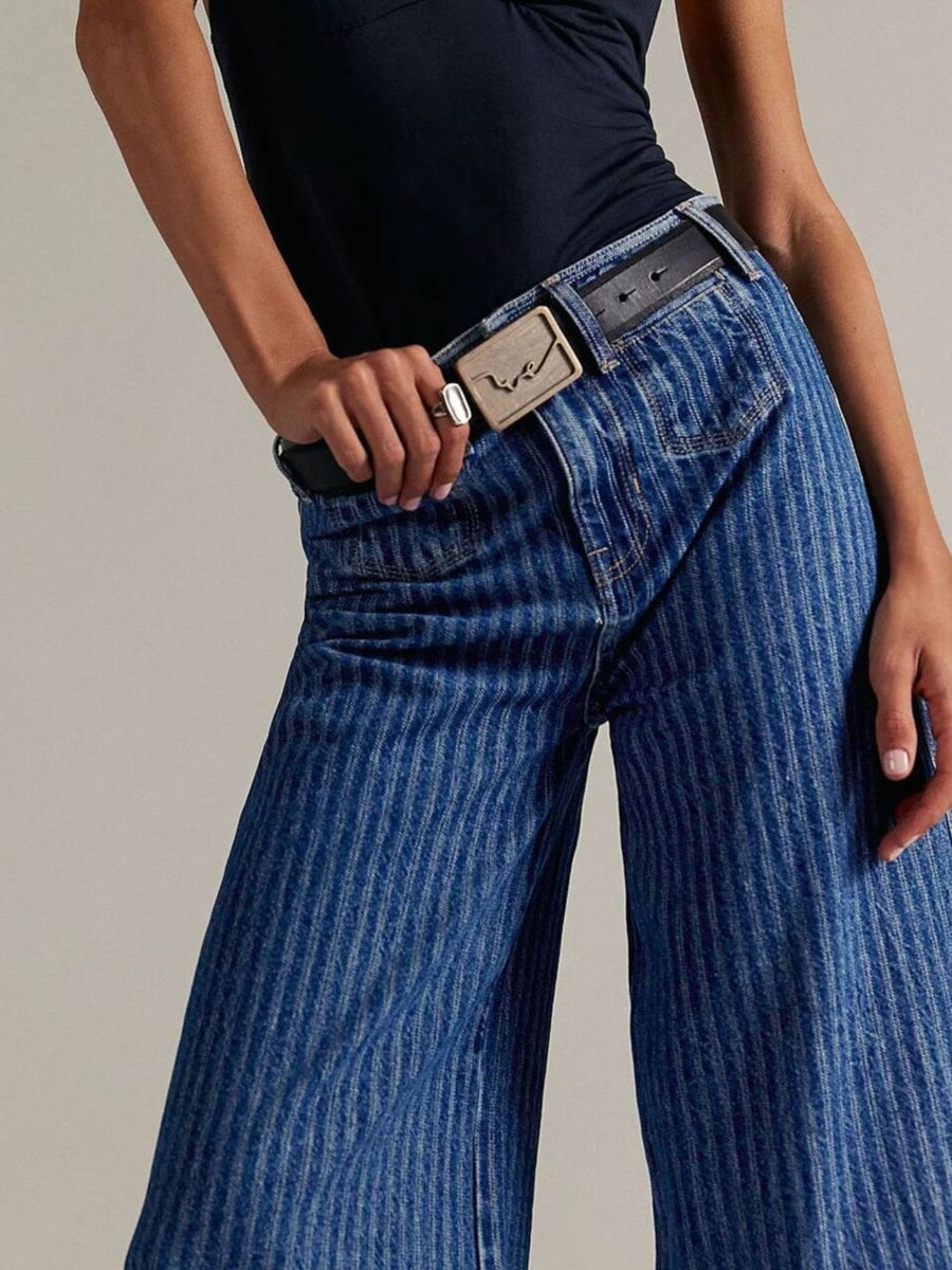 Person wearing blue corduroy pants with a belt on a neutral background