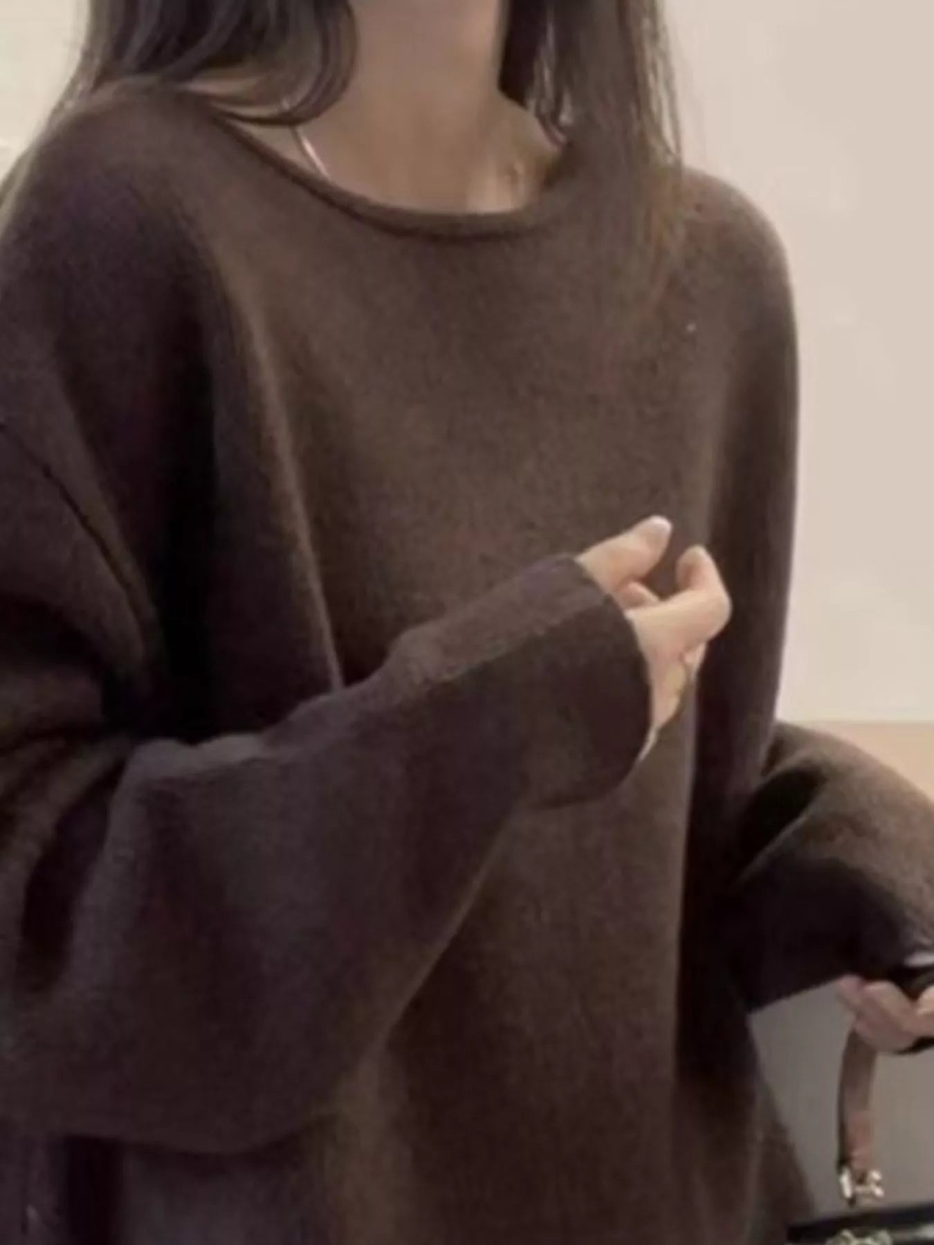 Person wearing a brown oversized sweater in a minimal indoor setting