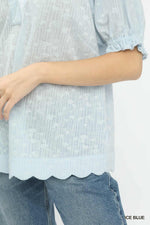 Light blue blouse with scalloped hem and rolled-up sleeves worn over jeans on a white background.