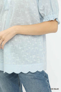 Light blue blouse with scalloped hem and rolled-up sleeves worn over jeans on a white background.