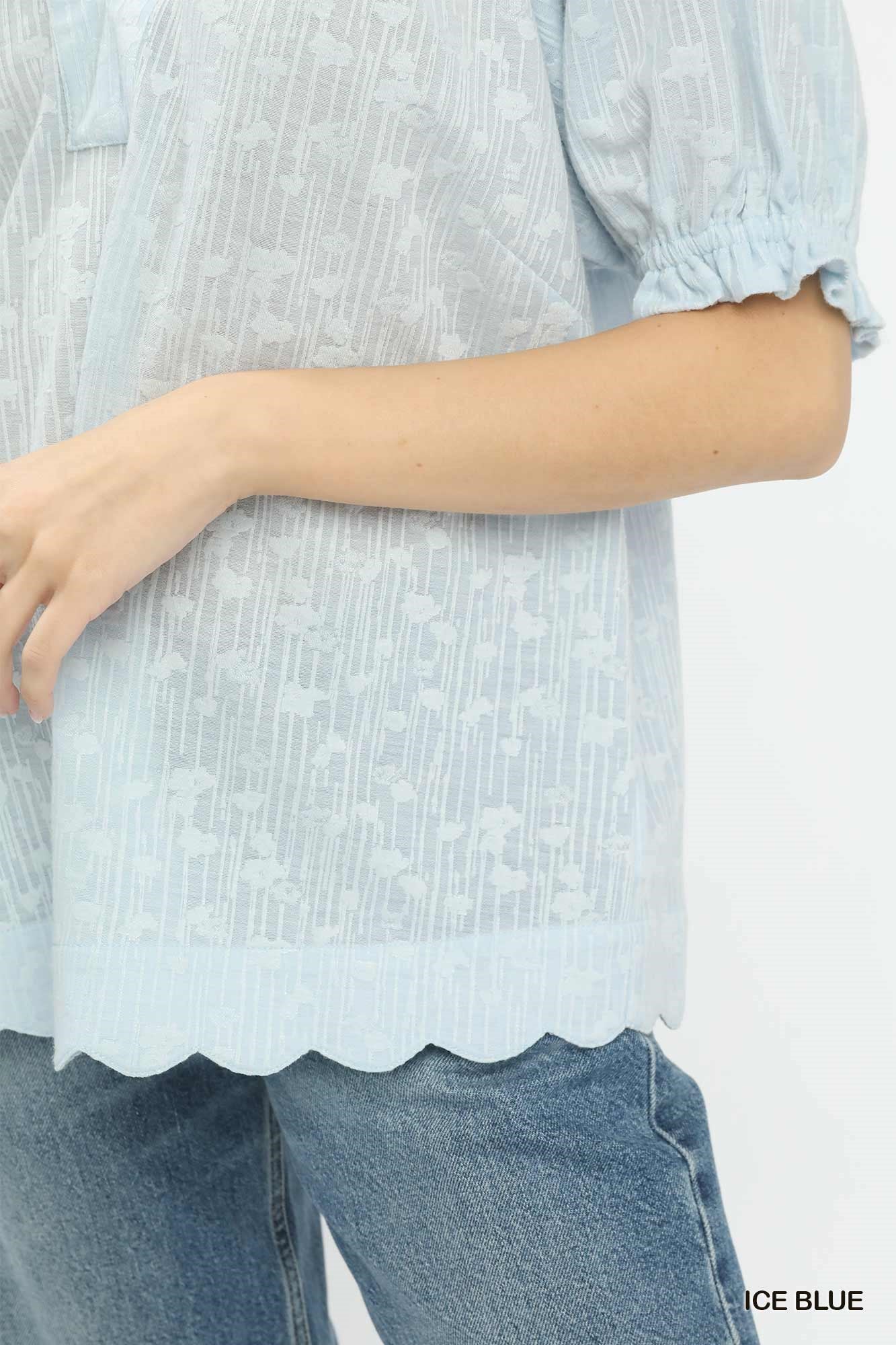 Light blue blouse with scalloped hem and rolled-up sleeves worn over jeans on a white background.