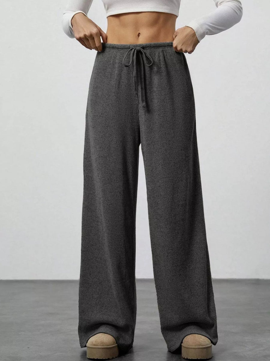 Person wearing gray wide-leg pants with a white top on a plain background