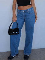 Person wearing blue jeans and a black top, holding a black handbag against a plain background