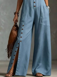 Person wearing a blue jumpsuit holding a brown leather bag against a neutral background
