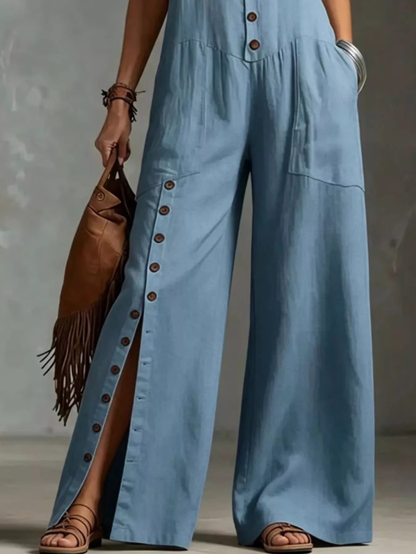 Person wearing a blue jumpsuit holding a brown leather bag against a neutral background