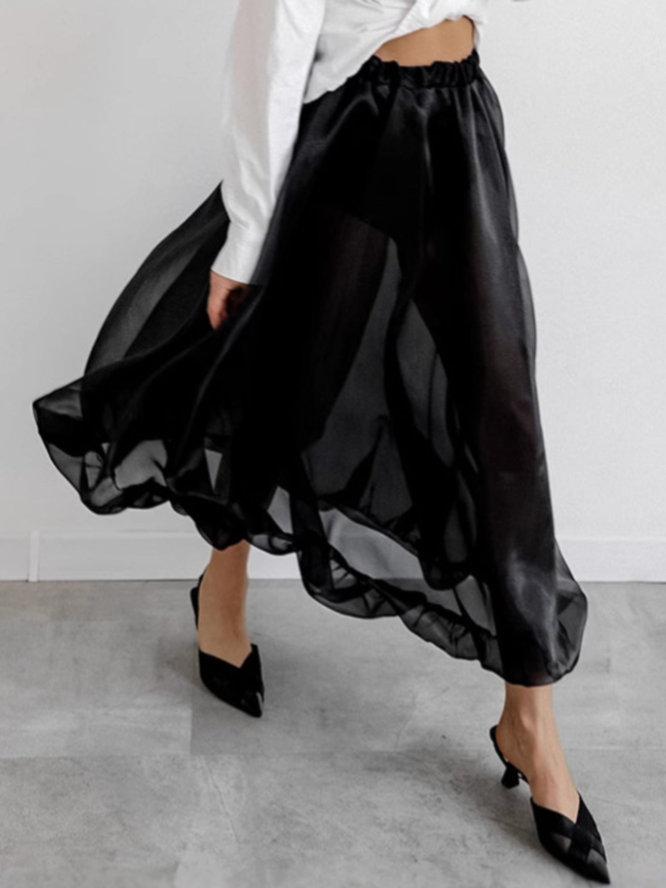Person wearing a black skirt and white shirt on a gray floor with white background